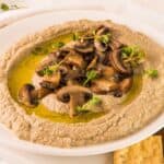 Hummus with mushrooms and crackers on a white plate.