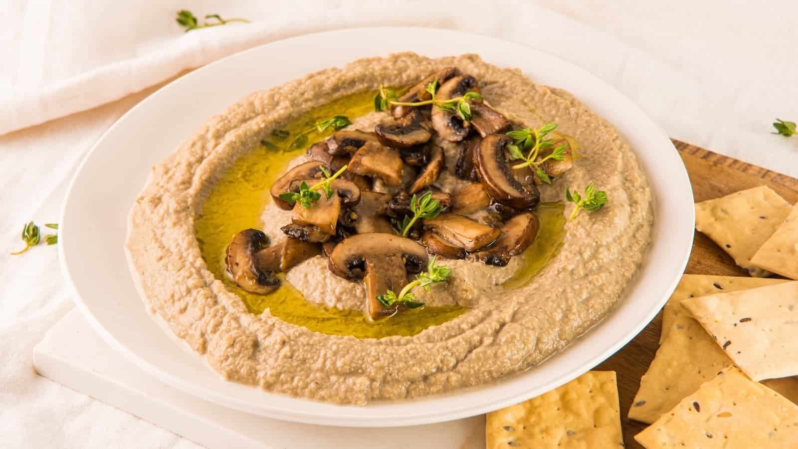 Hummus with mushrooms and crackers on a white plate.