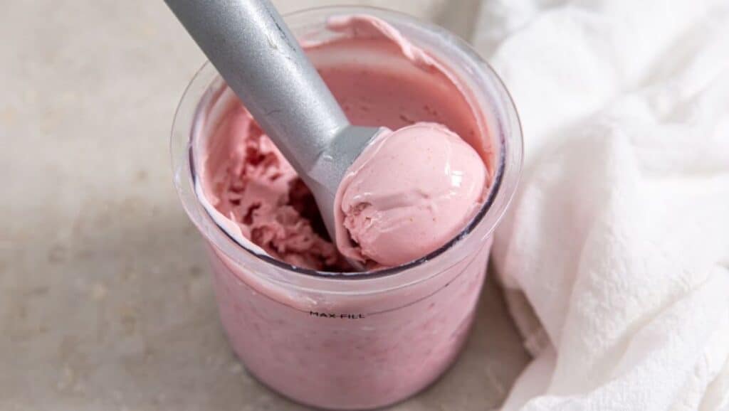 A scoop of pink strawberry ice cream in a blender with a spoon.