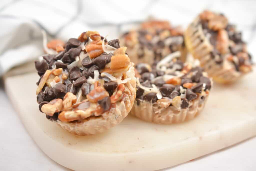 A close-up of peanut butter cups topped with chocolate chips and chopped nuts on a cutting board.