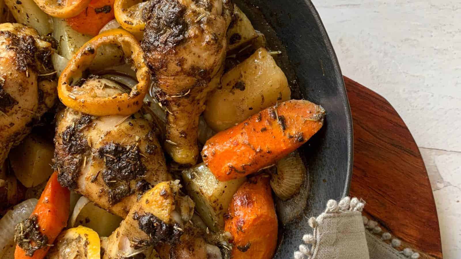 An iron skillet filled with hot chicken drumsticks and potatoes and carrots.