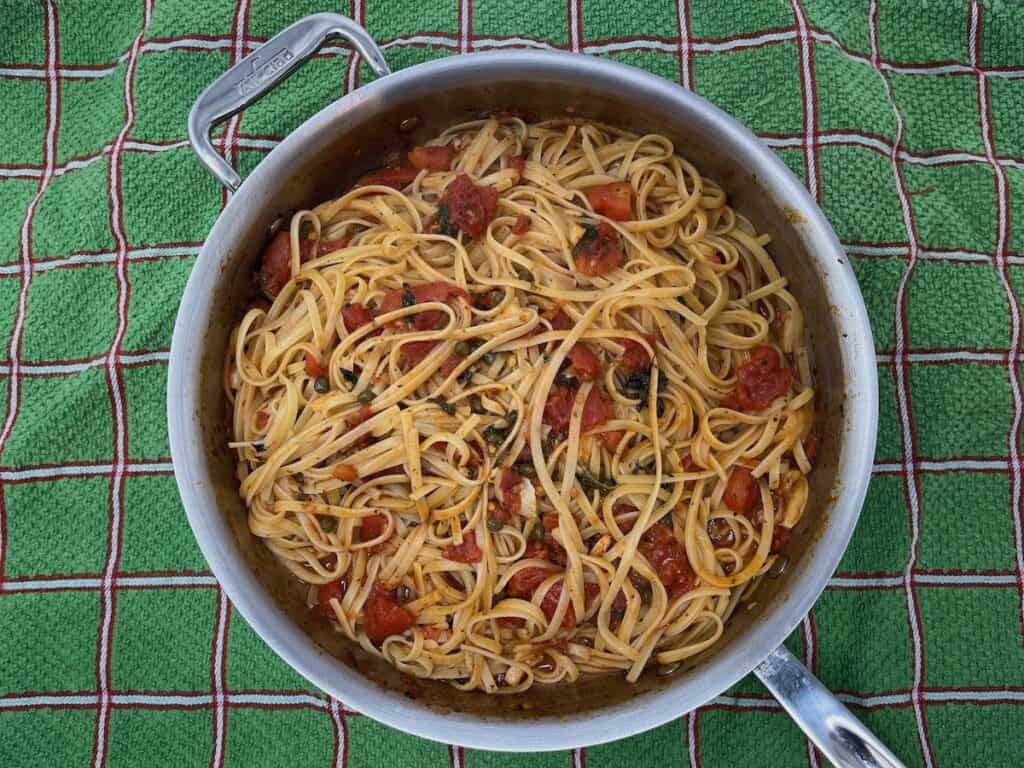 A pan full of pasta puttanesca on a tablecloth.