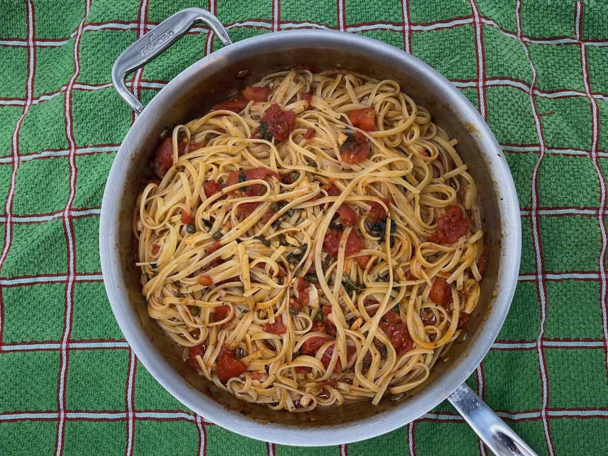 A pan full of spaghetti and tomatoes on a tablecloth.