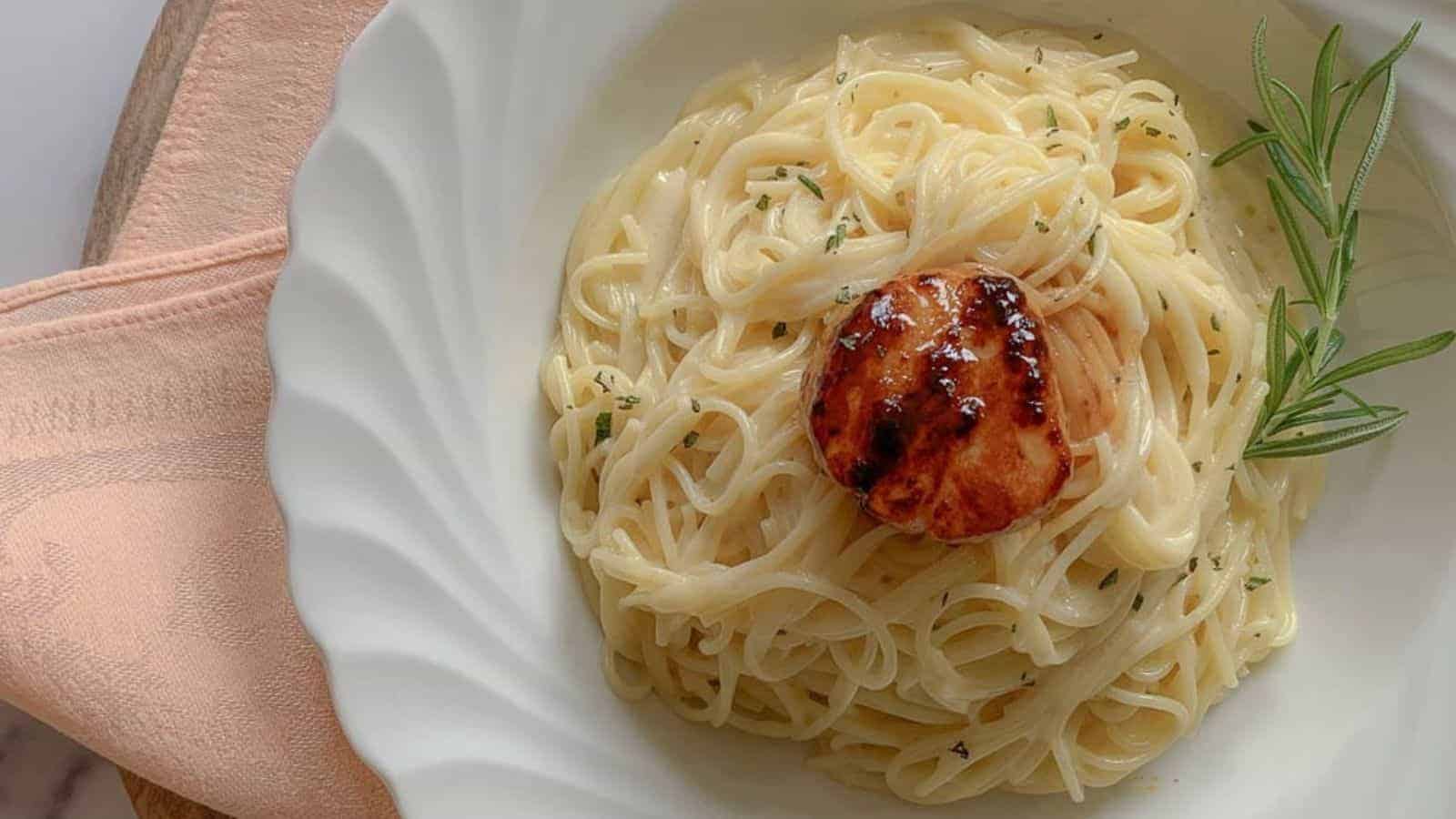 A pasta bowl filled with noodles in a butter and wine sauce with a single scallop on top.