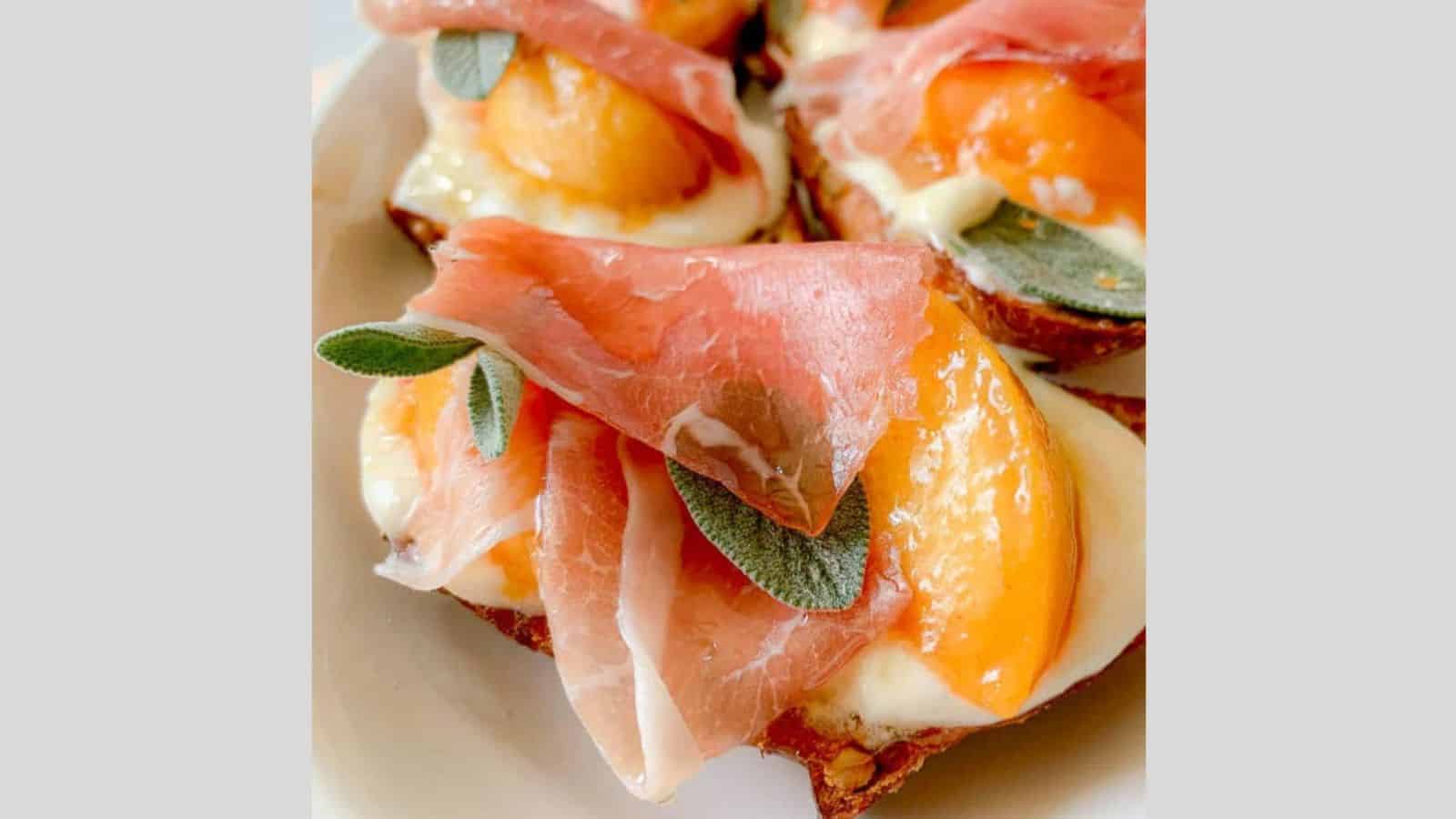 A bite sized piece of crisp bread piled high with prosciutto and peach slices and ricotta cheese.