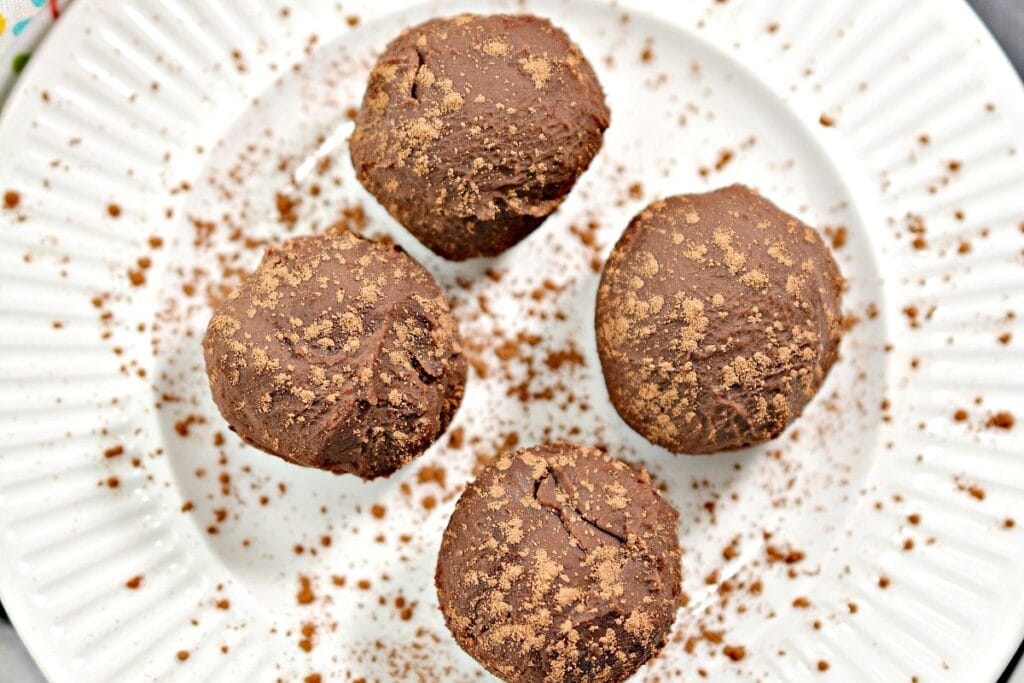 Three chocolate truffles on a white plate with cocoa powder sprinkled on top.