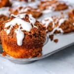 Freshly baked cinnamon muffins with white icing drizzle on a metal tray.