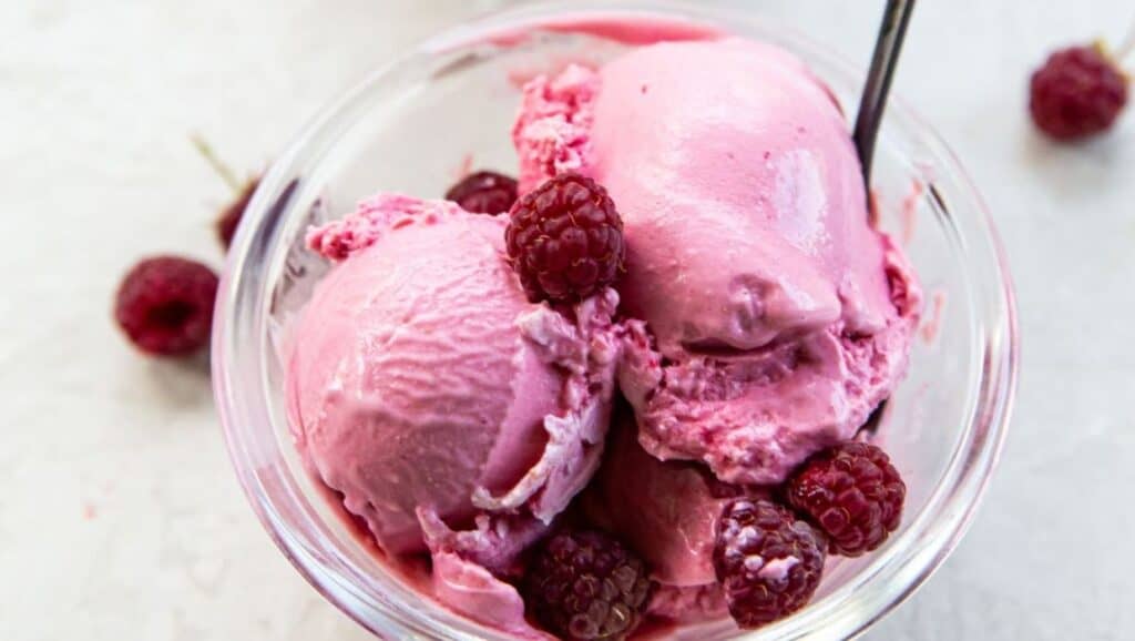 A bowl of ice cream with raspberries.