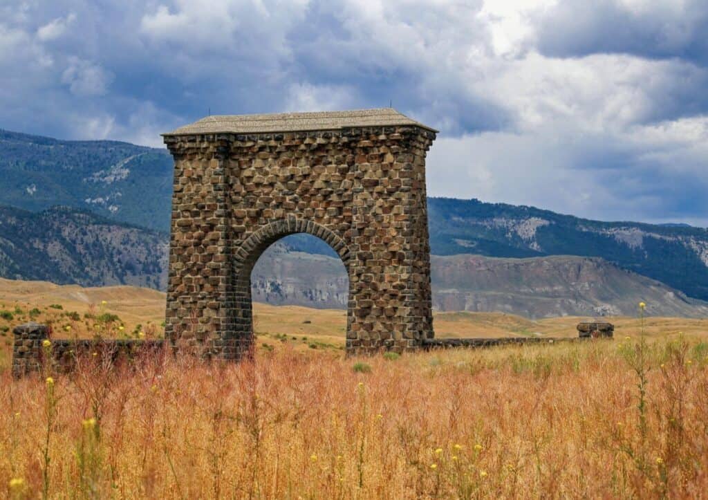 Stone archway standing alone in a field with mountains and a cloudy sky in the background.