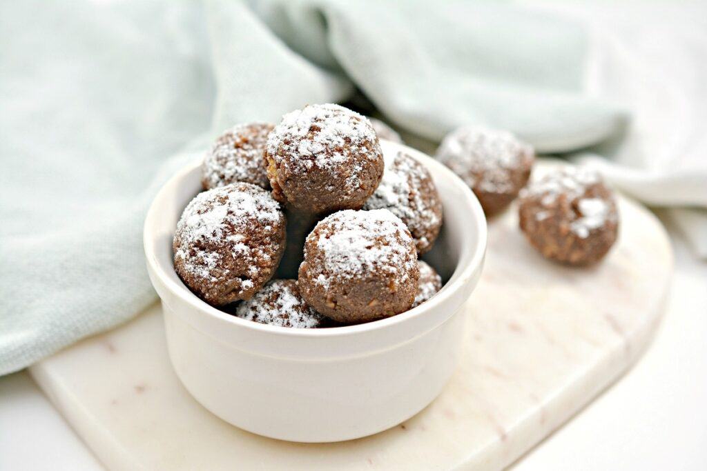 A bowl of chocolate truffles dusted with powdered sugar on a marble surface with a soft green cloth in the background.