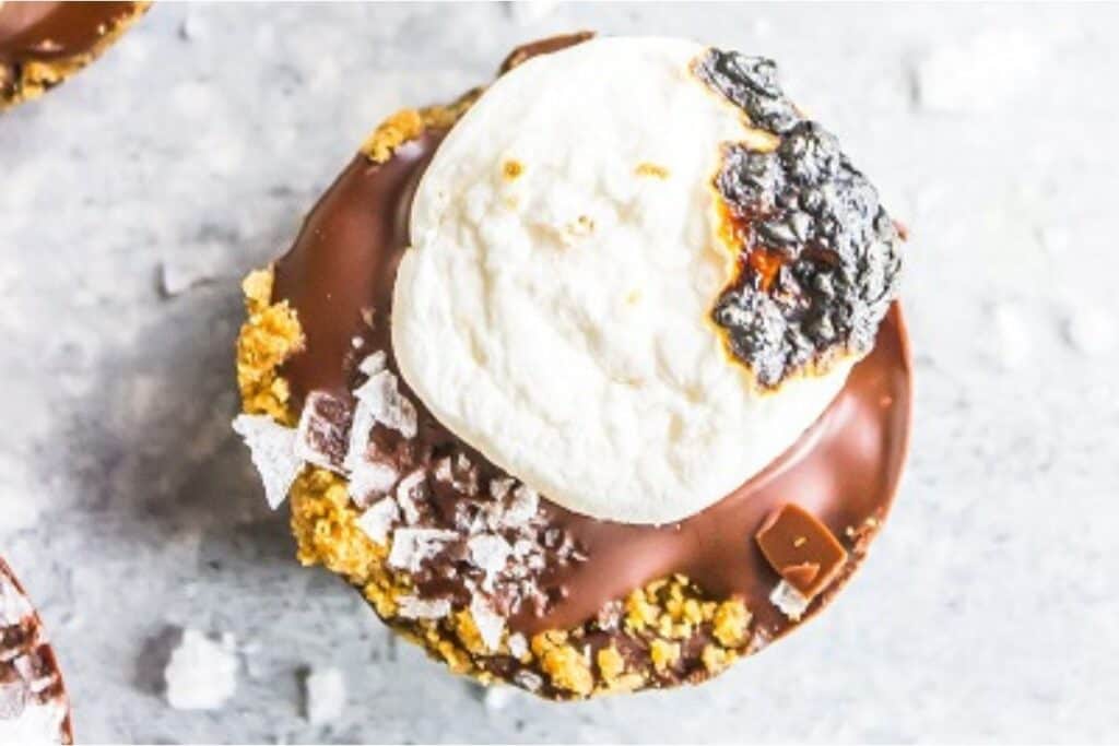 A gourmet s'mores cupcake with a marshmallow topping, chocolate glaze, and crumbled biscuit pieces.