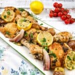 A platter of sheet pan lemon-rosemary chicken with lemon slices, herbs, and garnished with cherry tomatoes.