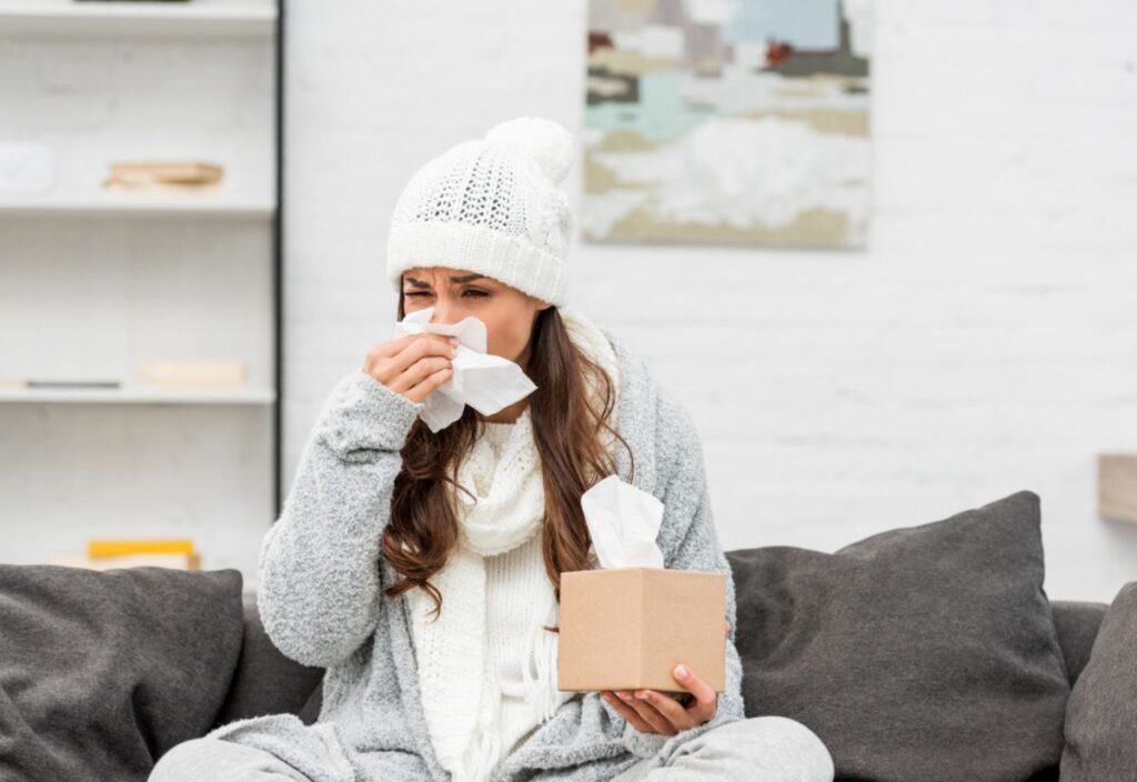 Woman with a cold blowing her nose on the couch.