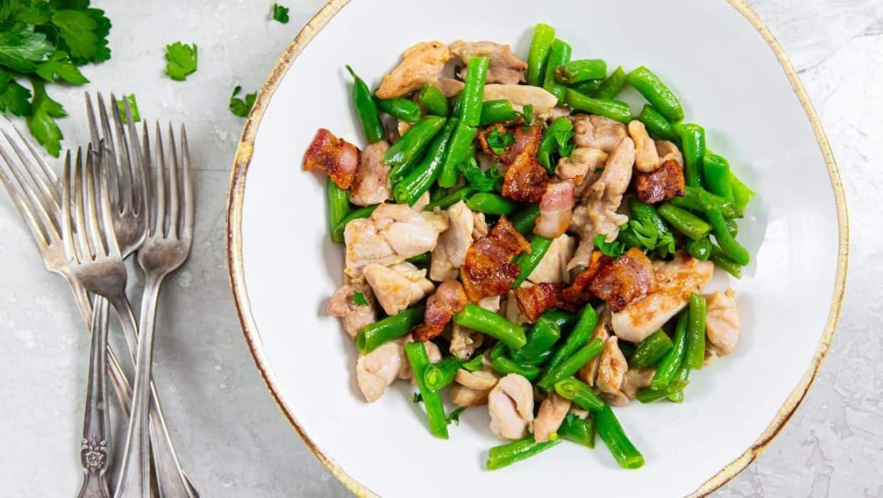 Skillet Chicken Thighs, Bacon, and Green Beans in a white bowl with a fork.