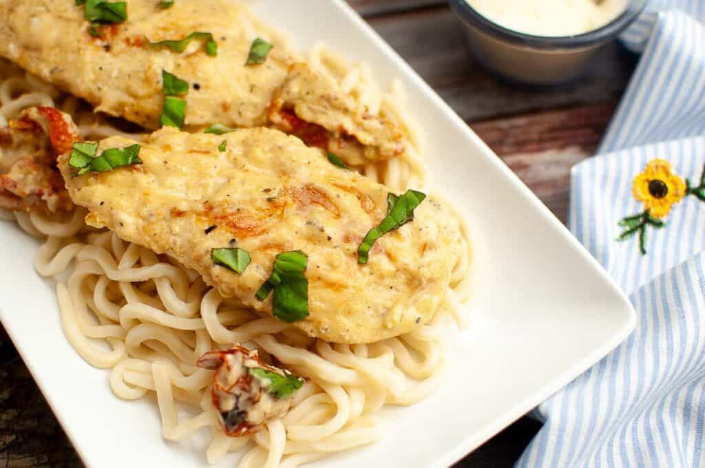 Grilled chicken breast served over a bed of pasta, garnished with fresh herbs.