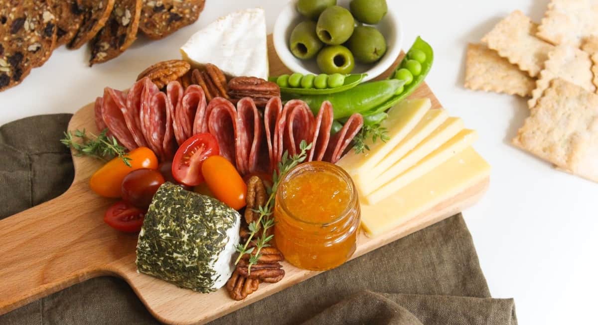 Cheese, meat, nuts, and veggies on a small charcuterie board. 