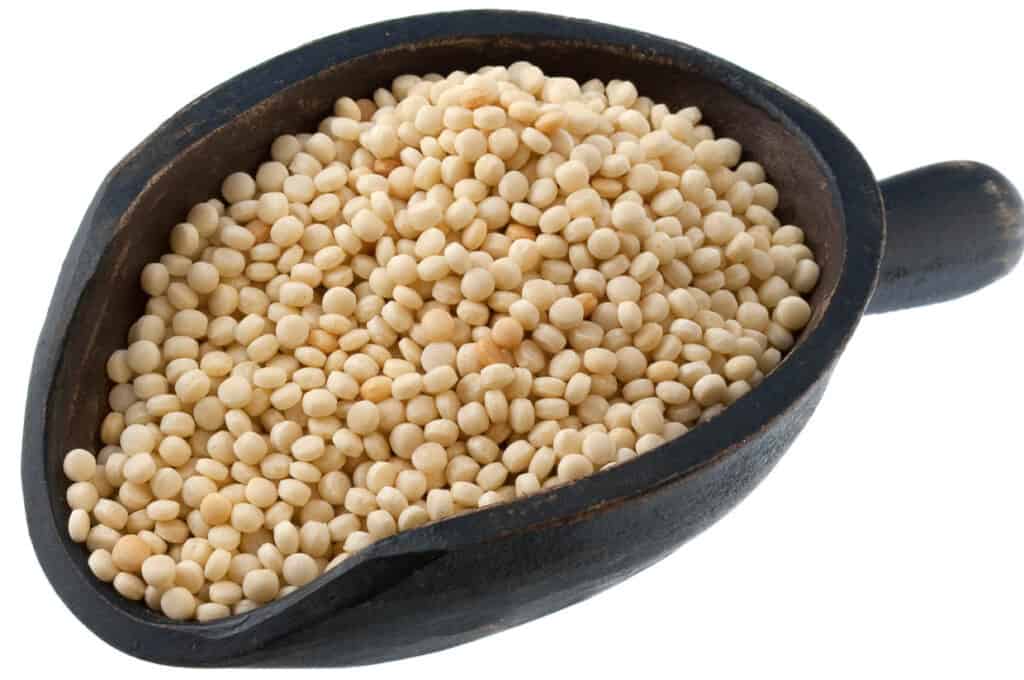 Couscous grains in a rustic scoop, isolated on a white background.