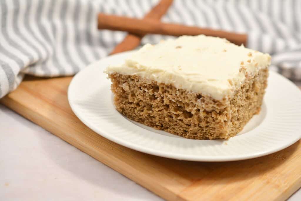 A slice of frosted cinnamon cake on a white plate.