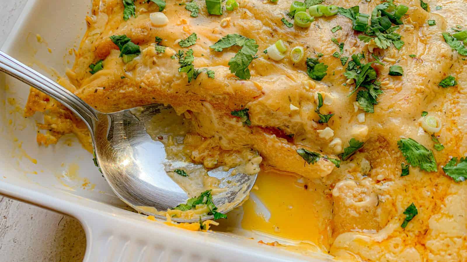 Enchiladas in a casserole dish, with chicken and cheese and a serving spoon.