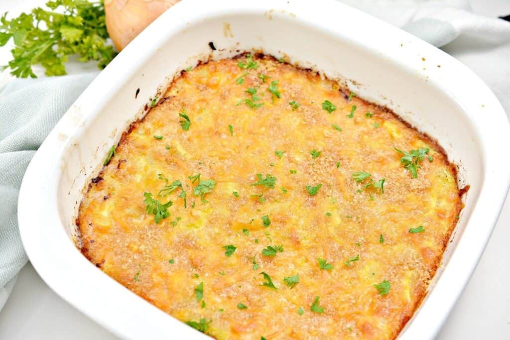 A freshly baked casserole topped with melted cheese and garnished with chopped herbs in a white baking dish.