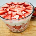 A bowl of strawberry trifle on a wooden surface.