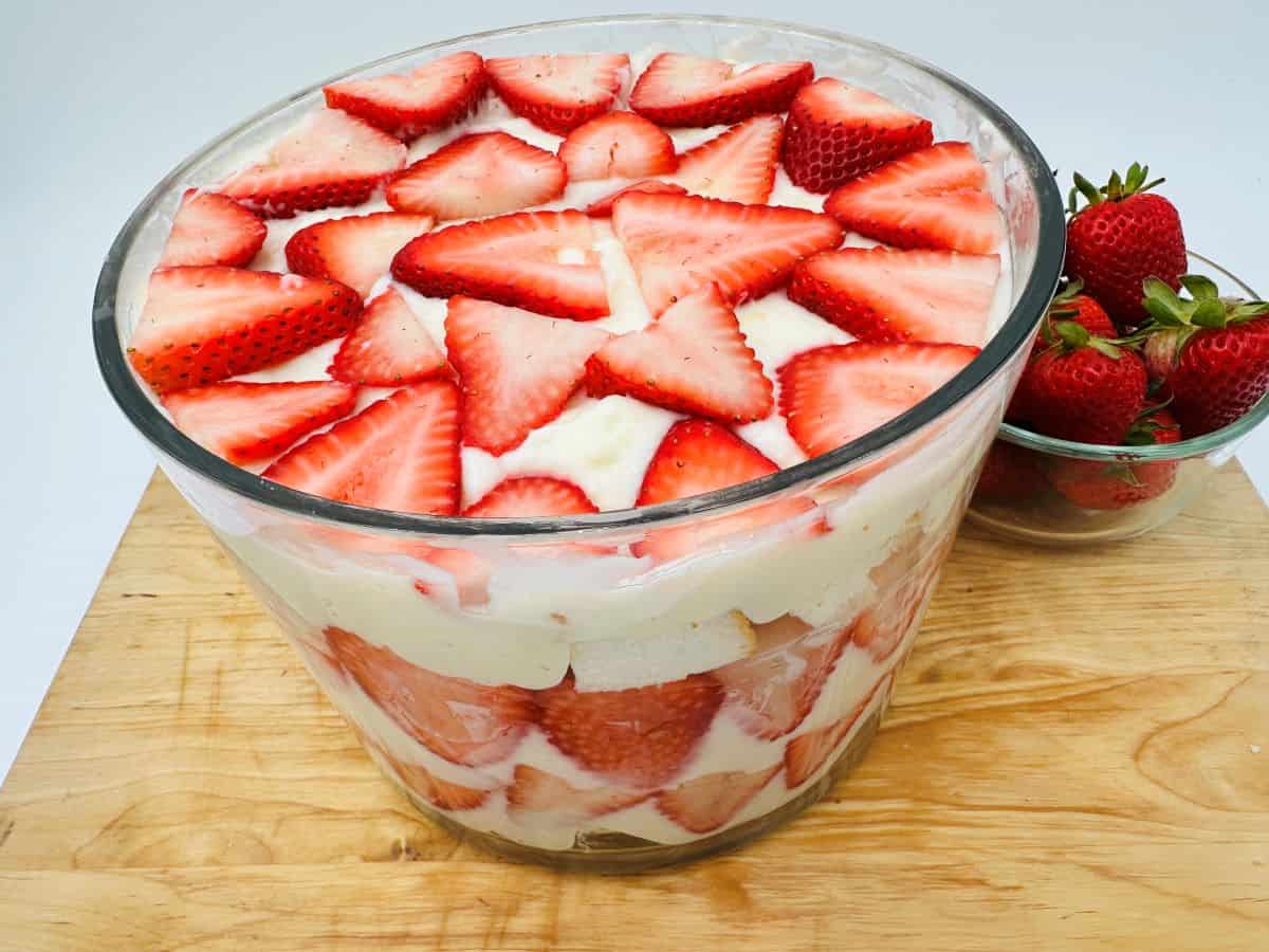 A bowl of strawberry trifle on a wooden surface.