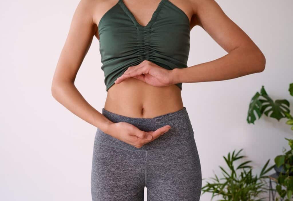A person in sportswear indicating a slim waistline, optimized for gut health, with their hands.