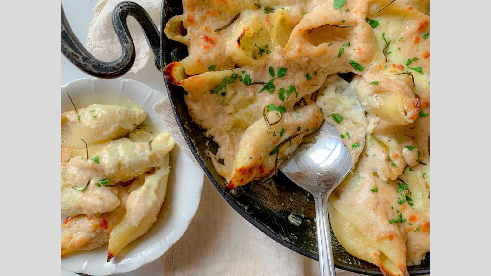 A cast iron pan filled with stuffed shells covered in cheese and a white sauce.