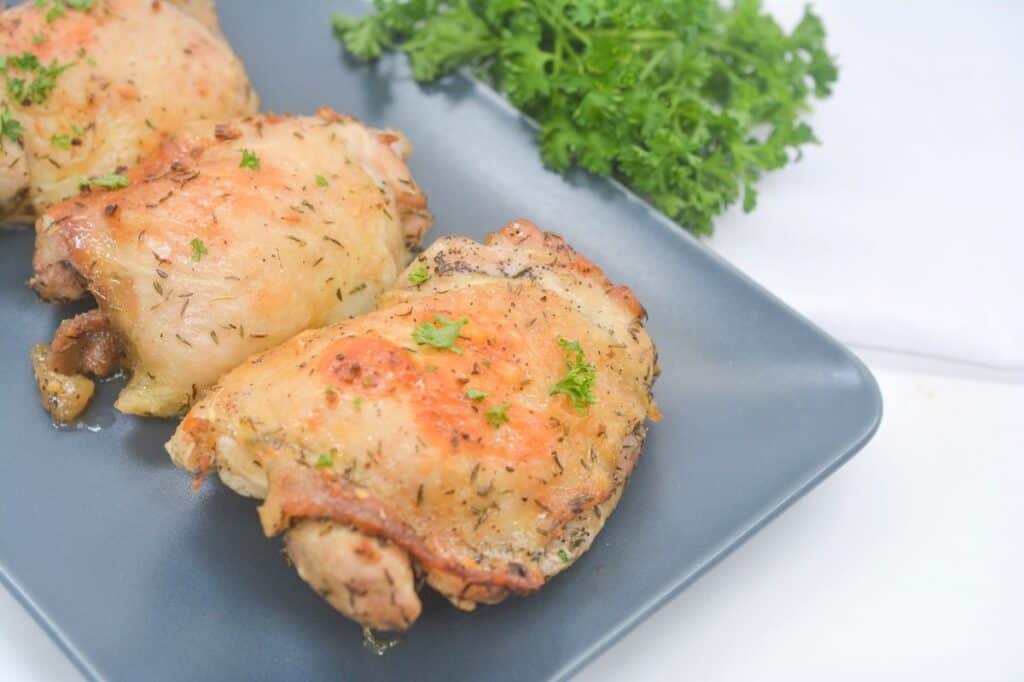 Herb-seasoned chicken thighs on a gray plate garnished with parsley.
