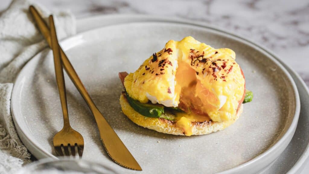 Eggs benedict with a runny yolk served on a plate with fork and knife, perfect for brunch recipes.