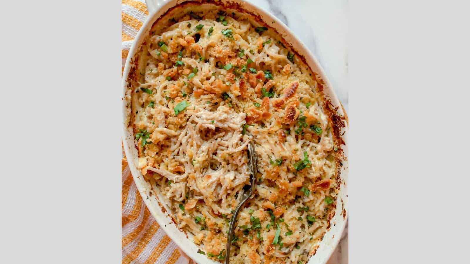 A casserole of turkey and noodles tetrazzini with a serving spoon resting in the center.