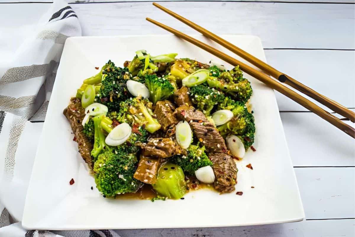 Beef and broccoli stir-fry with sesame seeds served on a white plate with chopsticks.