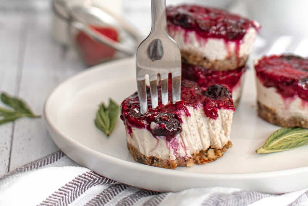 Mini cheesecakes with berry topping on a white plate with a fork taking a piece.