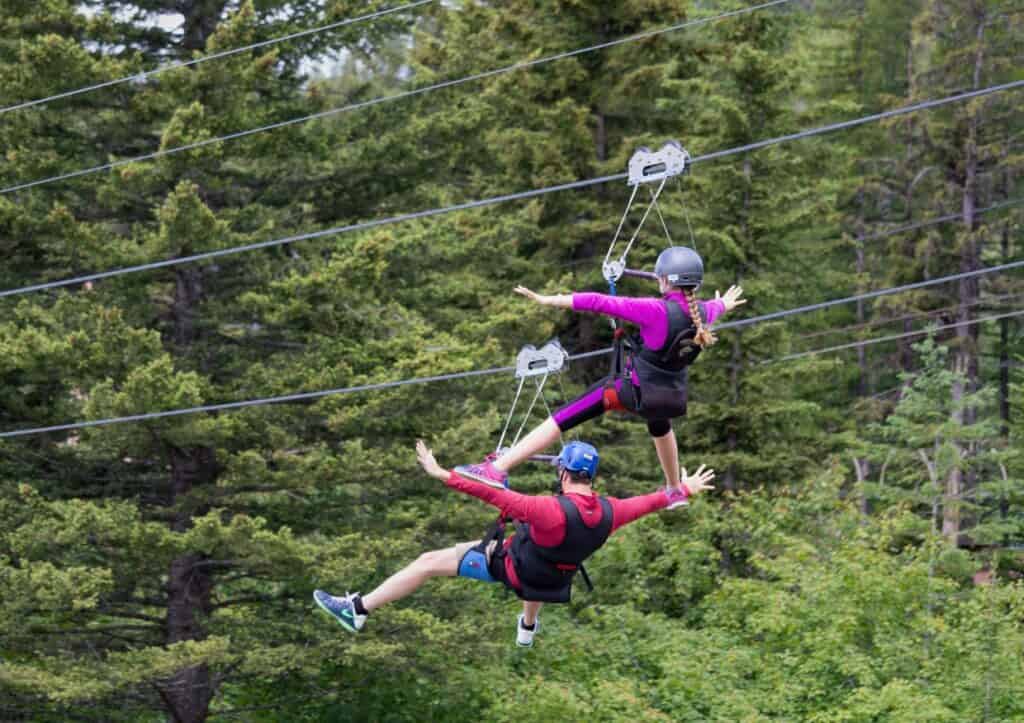 Two people ziplining through a forest.