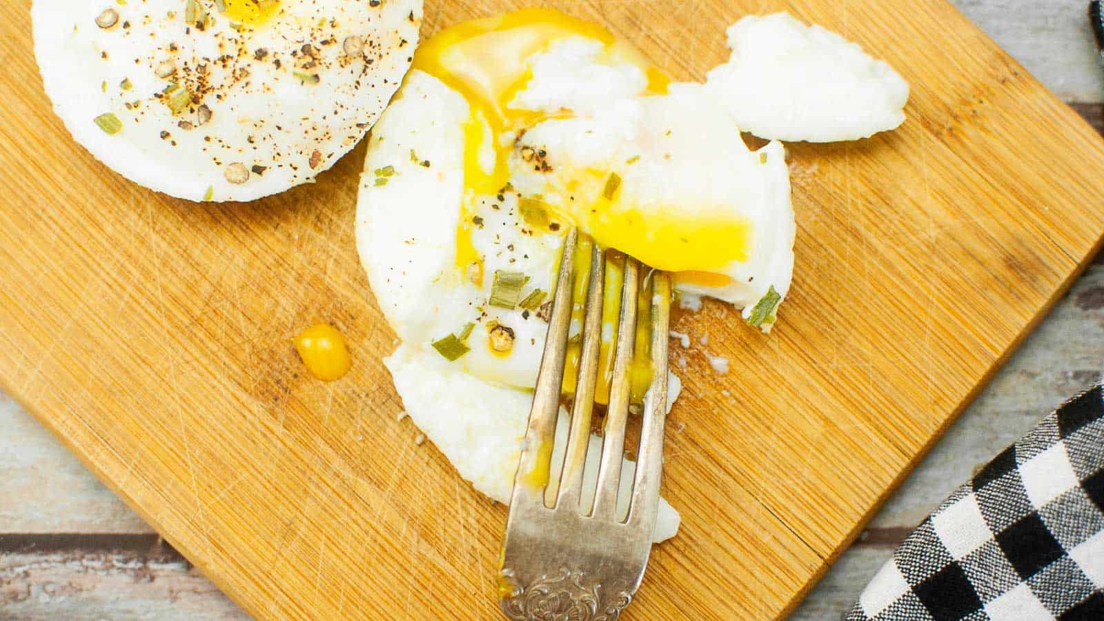 Poached eggs on a wooden cutting board with a fork.