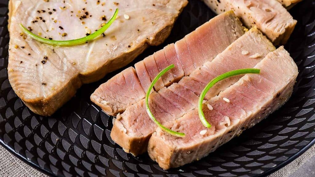 Sliced seared tuna steak garnished with green onion on a black plate.