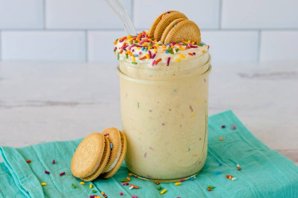 A milkshake with cookies and rainbow sprinkles in a jar.