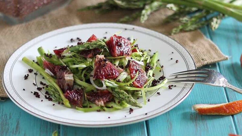 A plate of fresh asparagus salad with sliced blood oranges and sprinkled with black quinoa.