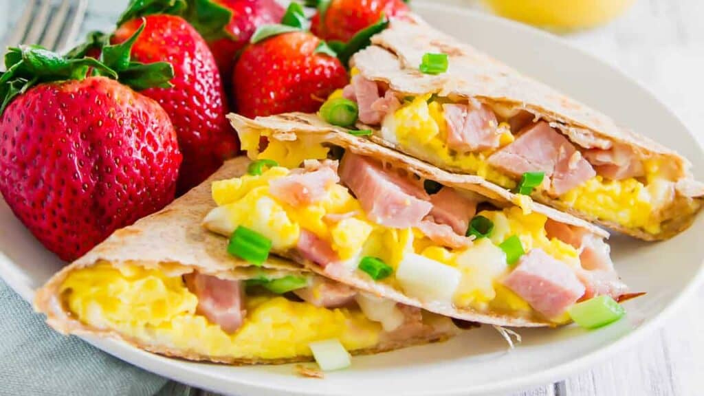 A plate of breakfast burritos with strawberries and ham.