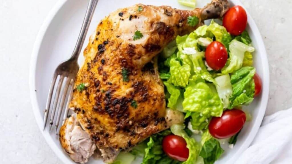 Grilled chicken leg served alongside a fresh garden salad with cherry tomatoes.
