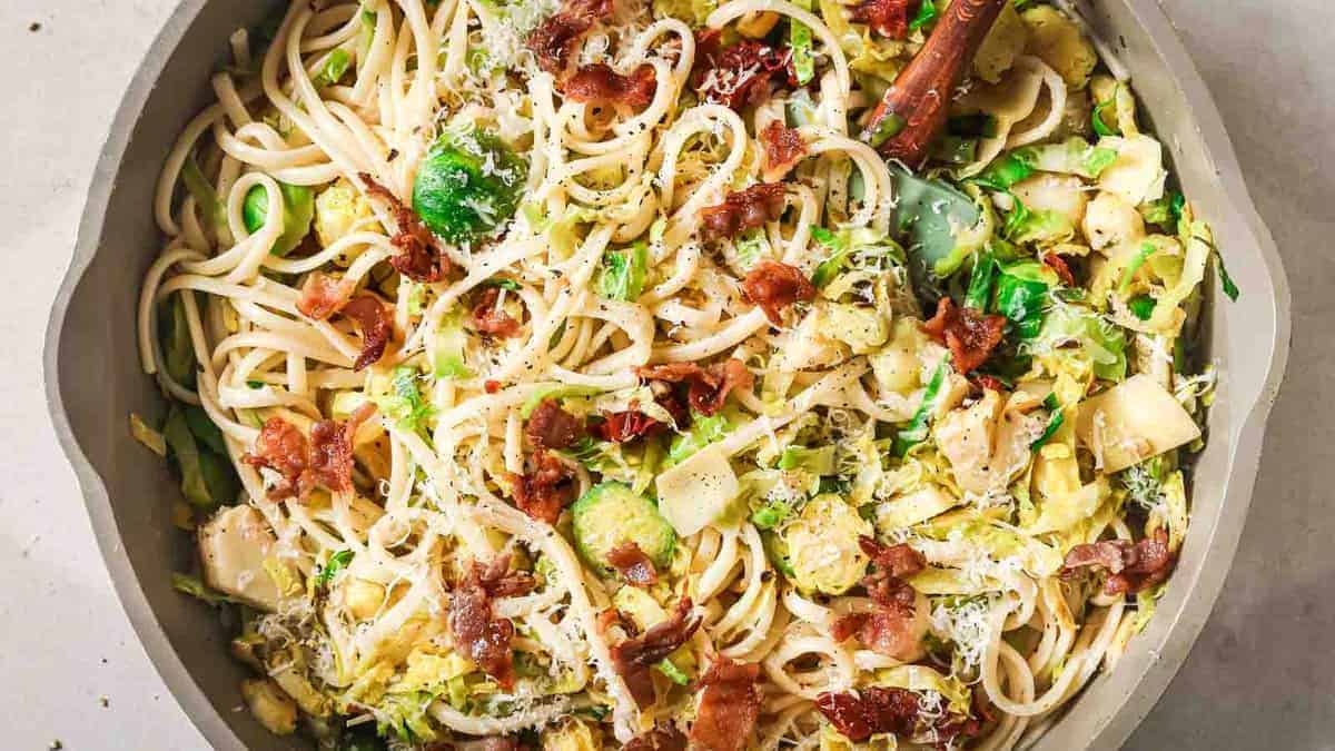A bowl of pasta with bacon and brussels sprouts.