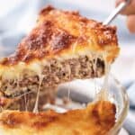 A slice of cheesy meat pie being lifted, showing melted cheese and meat layers.