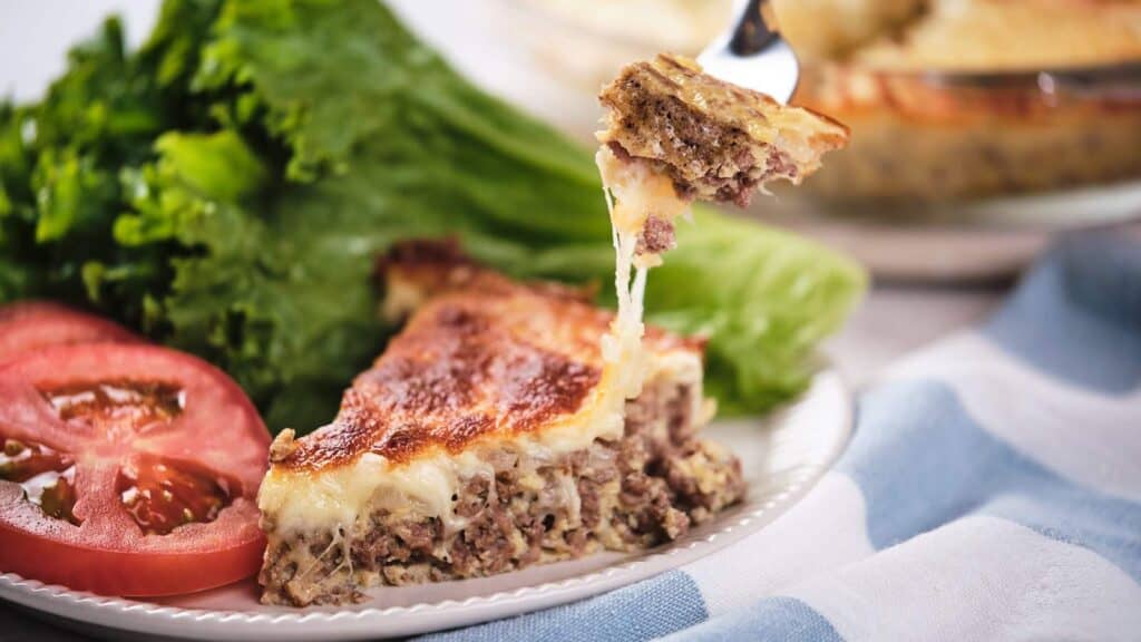 A slice of cheese-topped meat pie with a side of fresh tomatoes and lettuce.