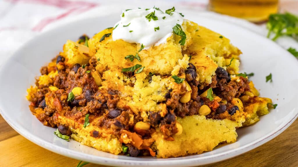 A plate of cornbread casserole topped with a dollop of sour cream and sprinkled with fresh herbs.