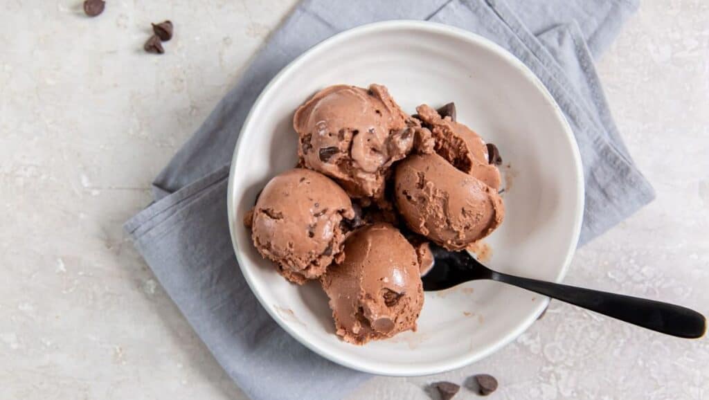 A bowl of chocolate chip ice cream with a spoon on a grey napkin.