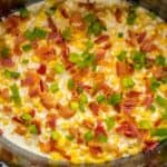 Creamy corn dish with bacon and green onions in a cooking pot.