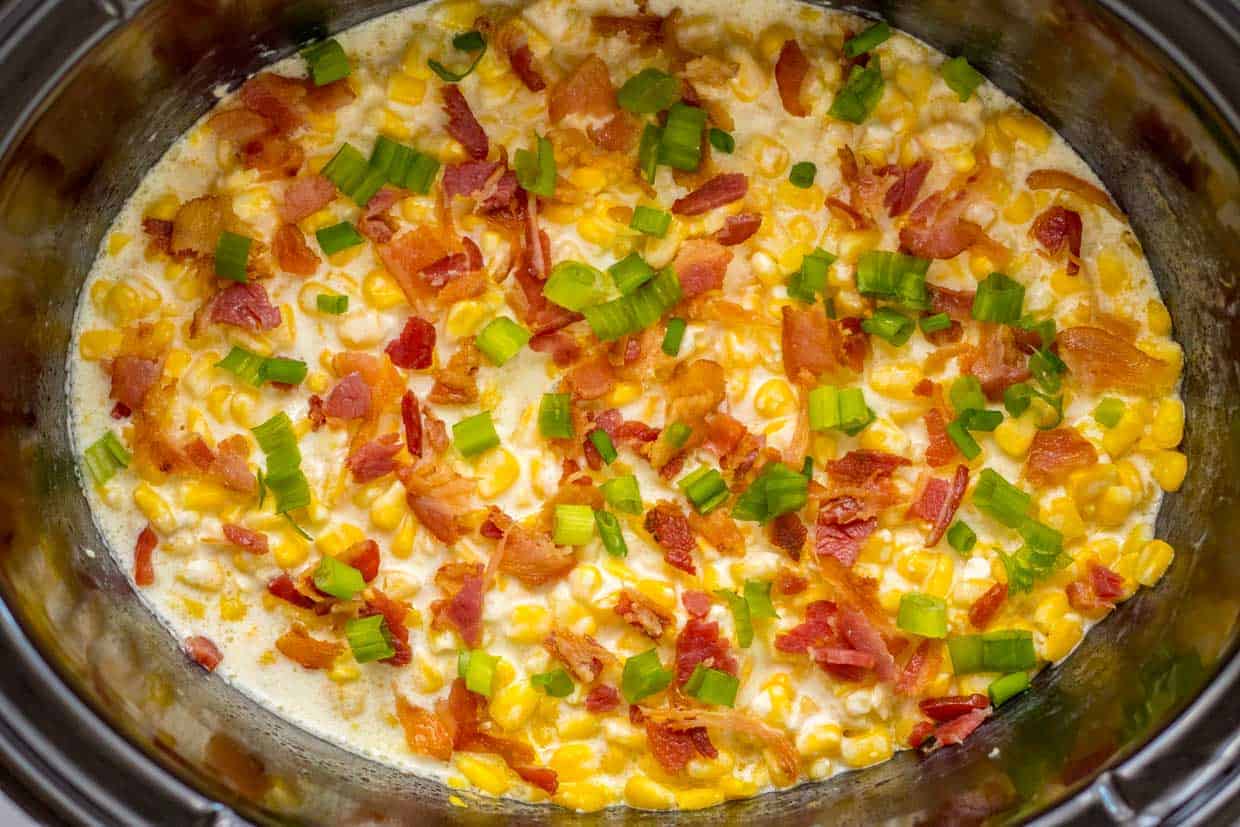 Creamy corn dish with bacon and green onions in a cooking pot.