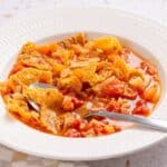 Bowl of hearty vegetable stew with a spoon on a light background.