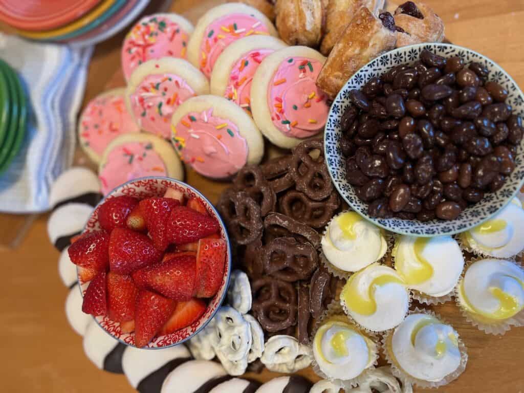An assortment of desserts including strawberries, chocolate-covered nuts, cupcakes, cookies, and pretzels on a table.