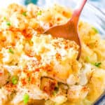 A bowl of creamy potato salad garnished with paprika and chopped herbs.